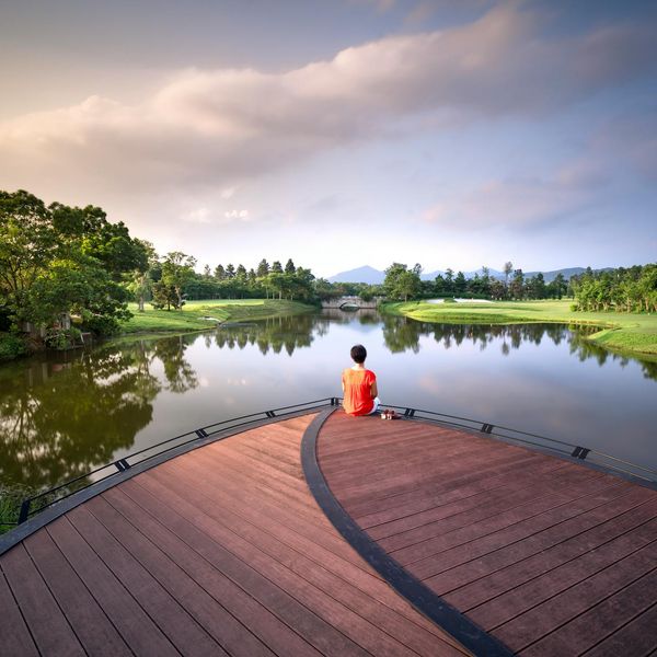 Person meditating peacefully outdoors near a calm lake at sunrise.
